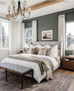 a bedroom with gray walls, white bedding and two lamps hanging from the ceiling