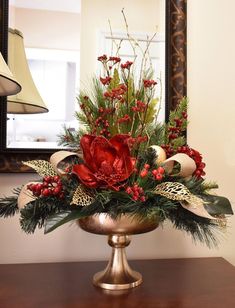 a christmas centerpiece with red flowers and greenery in a gold bowl on a table