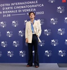 a man standing in front of a blue wall wearing a white jacket and black pants