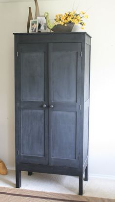 a black armoire sitting on top of a rug next to a vase with flowers