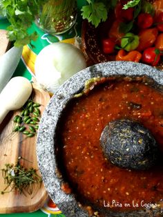 a bowl filled with red sauce next to vegetables and other foods on a cutting board