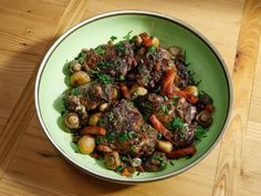 a bowl filled with meat and vegetables on top of a wooden table