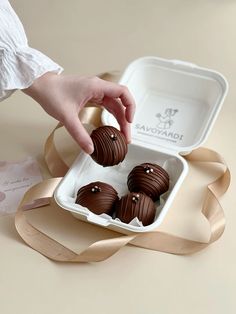 a person is picking up some chocolates from a white box on a table next to a brown ribbon