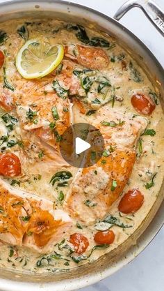 a pan filled with salmon and tomatoes on top of a stove next to a lemon wedge