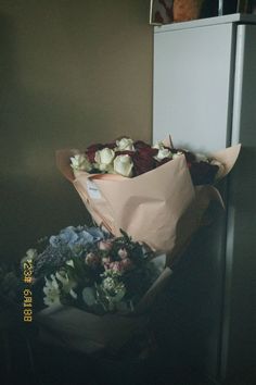 two bouquets of flowers sitting on top of a table in front of a refrigerator