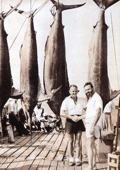 two men standing next to each other on a boat holding up large fish in front of them