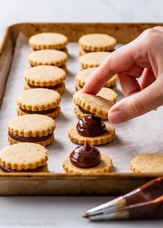 a person picking up some cookies from a baking sheet with chocolate on top and peanut butter on the bottom