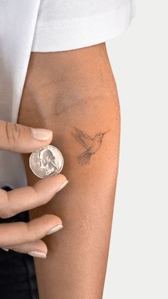 a woman's arm with a small tattoo on it and a coin in the other hand