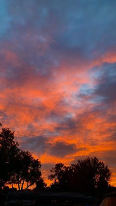 an orange and blue sky with trees in the background