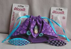 a purple bag sitting on top of a bed next to two small blue and white tags