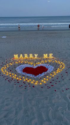 a heart - shaped sign on the beach that says marry me with candles in it