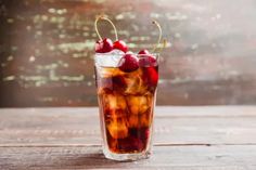 a glass filled with ice and cherries sitting on top of a wooden table next to a