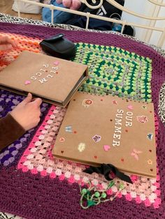 a person sitting on a bed with two notebooks in front of them and a crocheted blanket