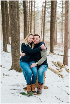 an engaged couple sitting on a log in the snow hugging and smiling at each other