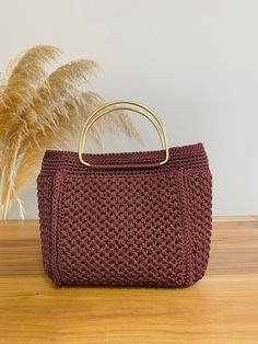 a red knitted purse sitting on top of a wooden table next to a plant