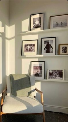 a chair sitting in front of a white wall with pictures on the shelves above it