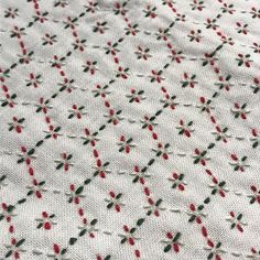 a close up view of a white fabric with red and green flowers on it,