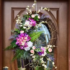 a wreath is hanging on the front door with pink and white flowers, greenery, and leaves