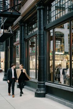 two people walking down the sidewalk in front of a store