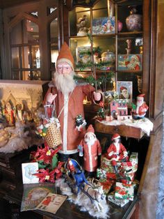 a santa clause standing in front of a table full of christmas decorations and gifts for sale