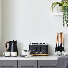 a kitchen counter with two coffee pots, toaster and cups on it next to a potted plant