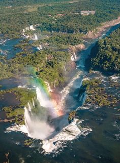 an aerial view of a waterfall with a rainbow in the middle and trees surrounding it