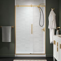 a bathroom with green walls and white tile on the floor, along with a gold framed shower door