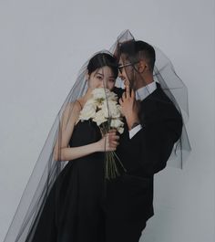 a man and woman under an umbrella with flowers in their hands, posing for the camera