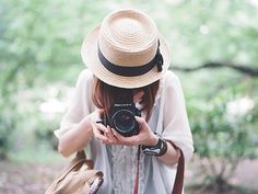 a woman in a hat taking a photo with a camera on the ground next to a brown bag