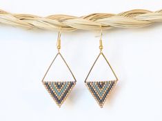 a pair of earrings hanging from a piece of woven string on a white background with a basket in the foreground