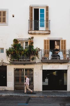 a man walking down the street in front of a building with balconies on it