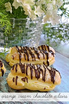 three pastries with chocolate drizzled on them sitting in front of flowers