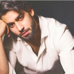 a man sitting down with his hand on his head and looking at the camera while wearing a white shirt