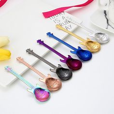 six colorful guitar shaped spoons are lined up on a white surface with pink ribbon