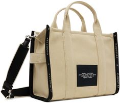 Canvas tote in beige. · Text-woven twill trim throughout · Twin rolled carry handles · Adjustable and detachable shoulder strap · Jacquard text and logo at face · Canvas loop at side · Logo patch at back face · Zip closure · Patch pockets at interior · Zip pocket · Unlined · Logo-engraved silver-tone hardware · H10 x W13.25 x D6.5 Supplier color: Warm sand Double Handle Bags With Logo Strap For Shopping, Shopping Bags With Logo Strap And Double Handle, Canvas Bags With Logo Strap For Travel, Canvas Travel Bag With Logo Strap, Travel Canvas Bag With Logo Strap, Beige Travel Bag With Logo Strap, Marc Jacobs Tote, White Tote Bag, Craft Tote Bag