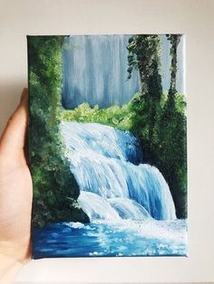 a painting of a waterfall being held up by a person's hand in front of it