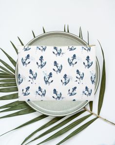 a blue and white cactus print zipper pouch on a plate with palm leaves around it