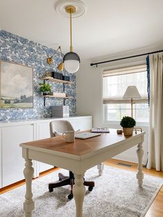 an office with blue and white wallpaper on the walls, wooden desk and chairs