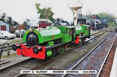 a green and red train engine sitting on the tracks next to a water tower at a station