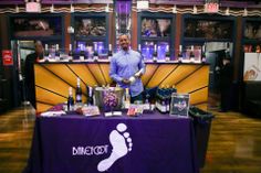 a man standing in front of a purple table covered with wine bottles and other items