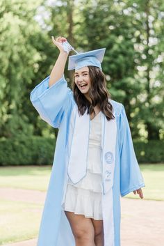 a woman in a blue graduation gown and cap is holding her hand up to the sky