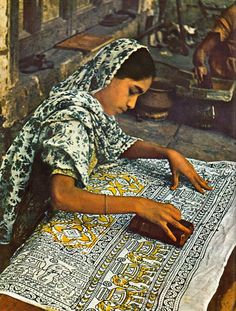 a woman sitting on top of a rug next to a man in an alleyway