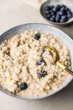 a bowl of oatmeal with blueberries in it and a gold spoon