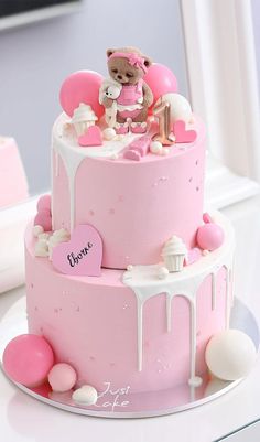 a pink cake with white icing and teddy bear on top, sitting on a table