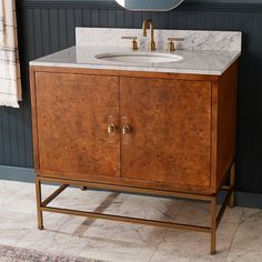 a bathroom vanity with marble counter top and gold faucet, in front of a blue wall