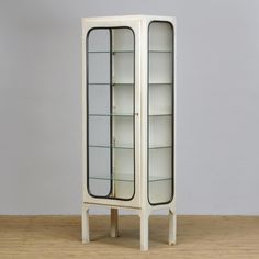 a tall white cabinet with glass doors on the top and bottom shelves, in front of a gray wall