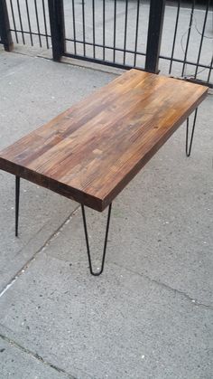 a wooden table sitting on top of a sidewalk next to a metal fence and gate