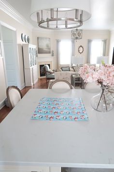 a dining room table with white chairs and pink flowers in a vase on the table