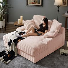 a woman sitting on top of a pink couch in a living room next to a lamp