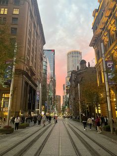 people are walking down the street in an urban area at sunset or dawn with tall buildings on either side